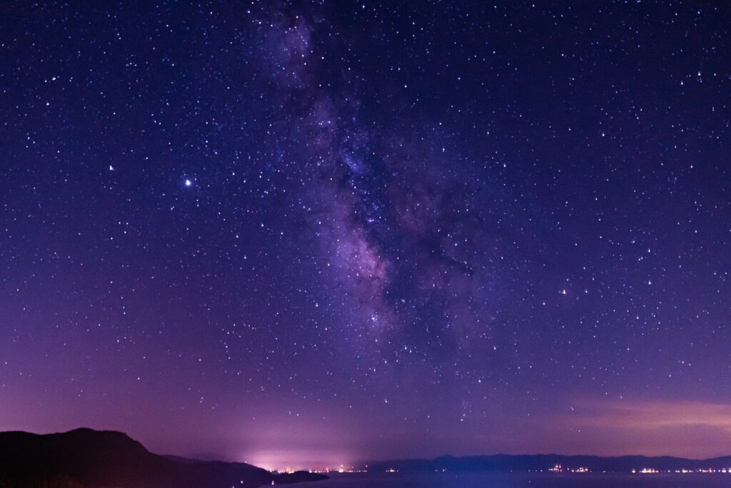 Fotografia noturna com céu estrelado e lago tranquilo.